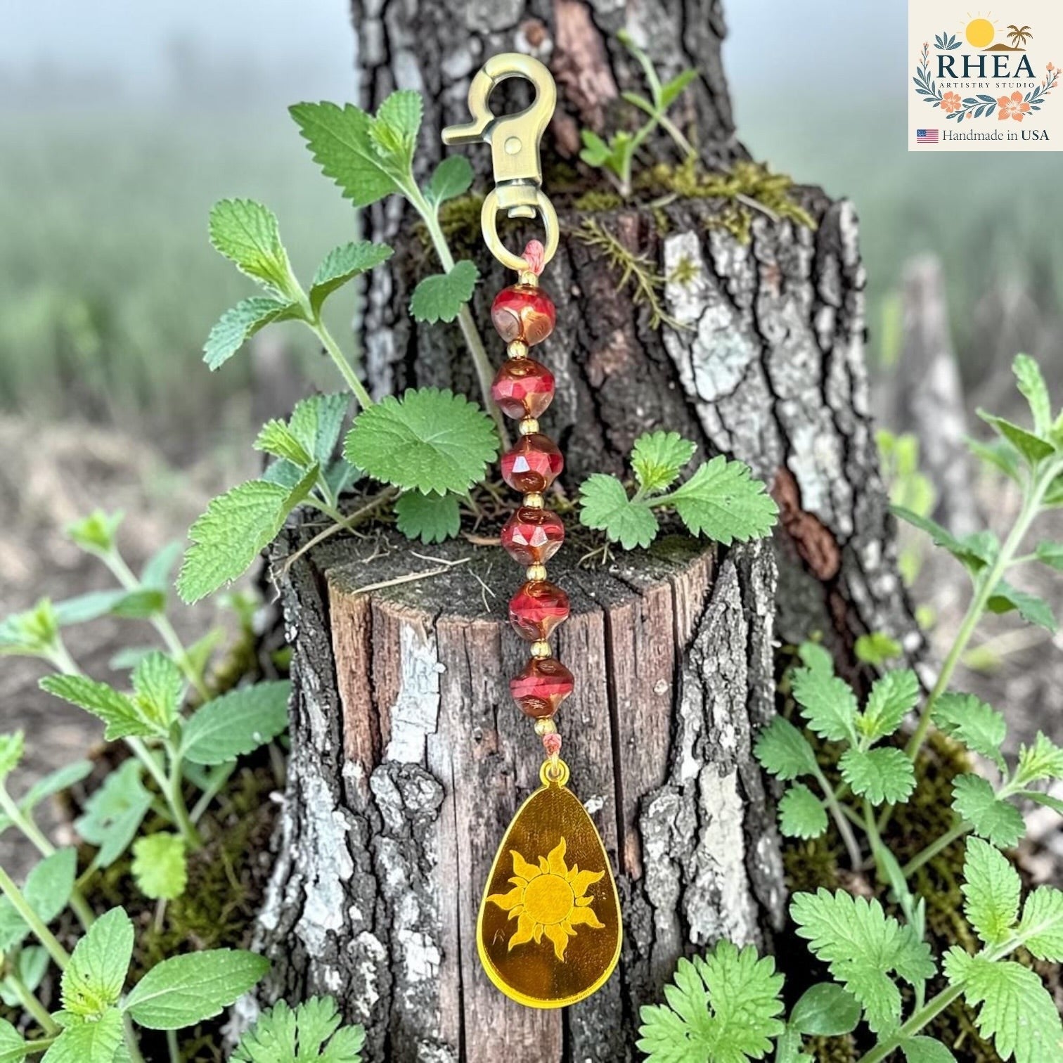 Rhea Artistry Studio artisan bag charm with red Czech glass beads, brass accents, and a hand-painted sun pendant.