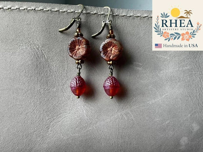 Rhea Artistry Studio handmade Czech glass earrings with rusty pink floral beads and brick orange acorn charms, brass hardware, 1.5-2 inches long.
