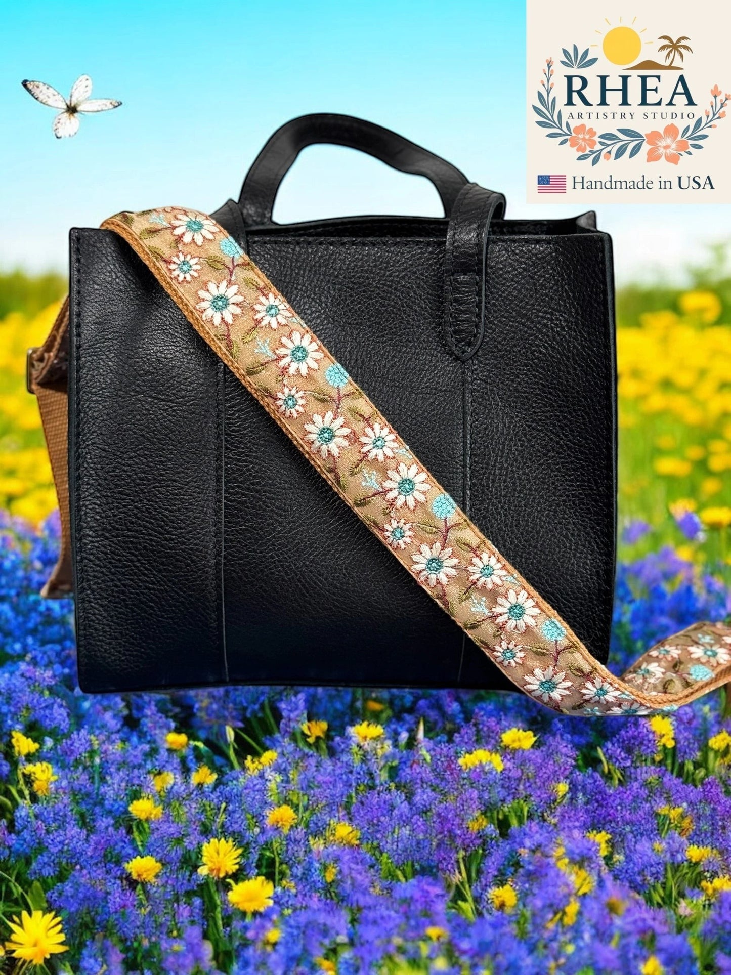 Rhea Artistry Studio 1.5-inch crossbody strap with embroidered white and blue daisies on tan fabric, adjustable length, brushed brass hardware.