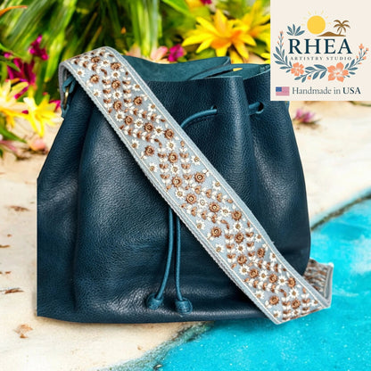 Rhea Artistry Studio dusty blue crossbody strap with bronze floral embroidery, 2-inch width, adjustable length.