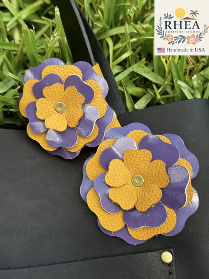 Rhea Artistry Studio eggplant and yellow double leather flower accessory with brass rivets on a black bag.