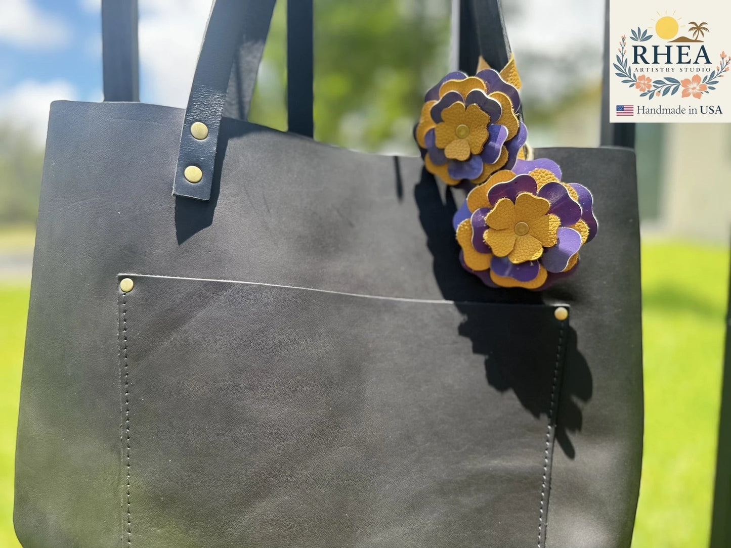 Rhea Artistry Studio eggplant and yellow double leather flower charms with brass rivets on a black leather tote bag.