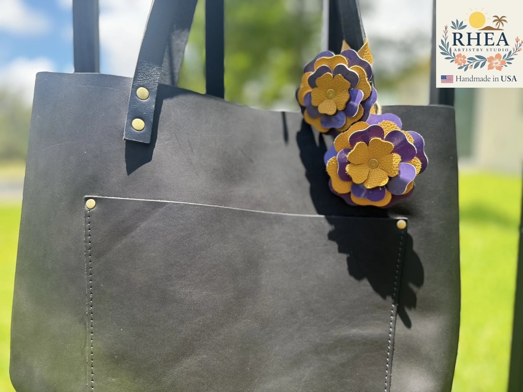 Rhea Artistry Studio eggplant and yellow double leather flower charms with brass rivets on a black leather tote bag.