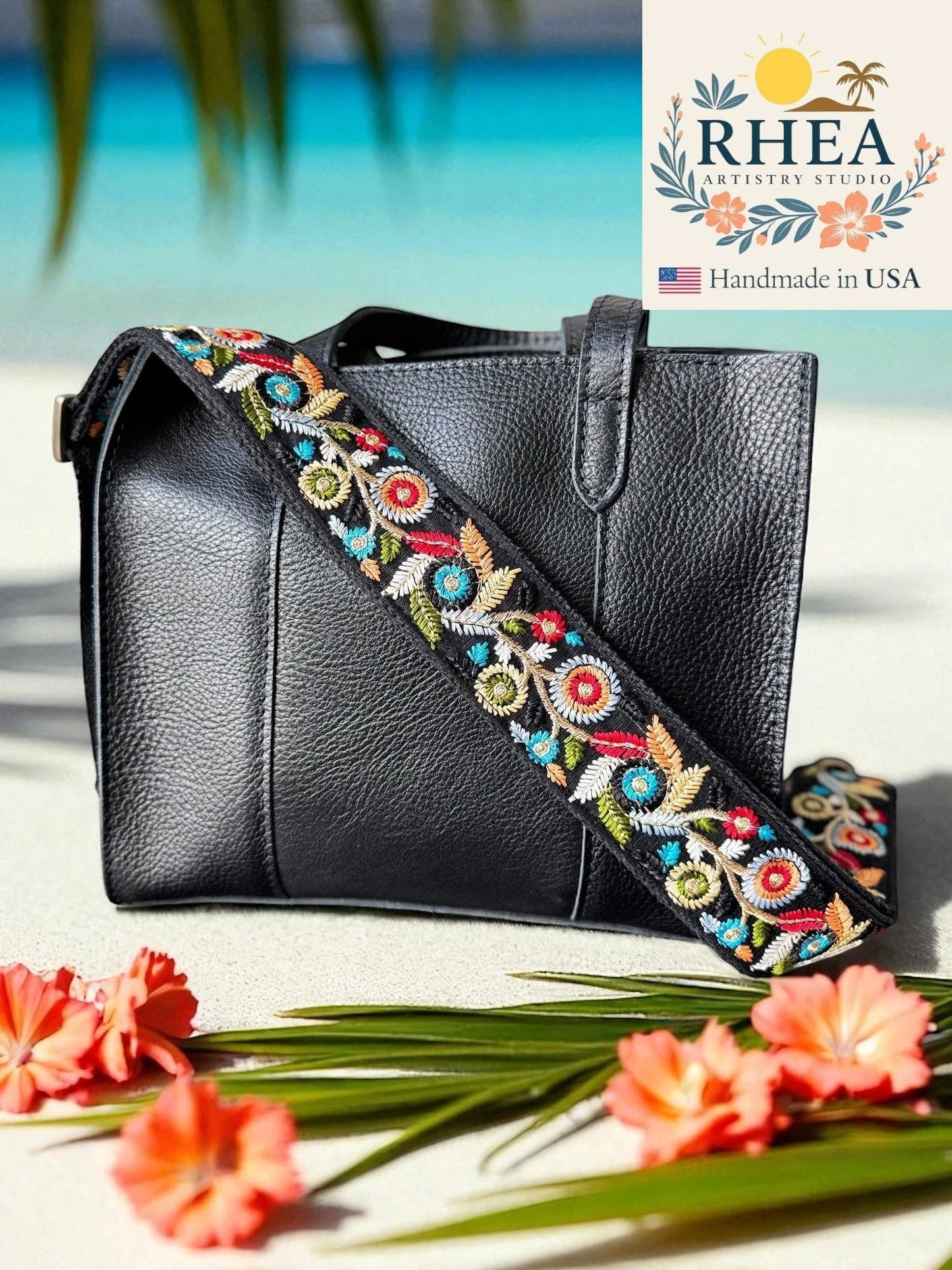 Rhea Artistry Studio black crossbody bag with a 2-inch wide adjustable strap featuring colorful floral embroidery and brushed brass hardware.