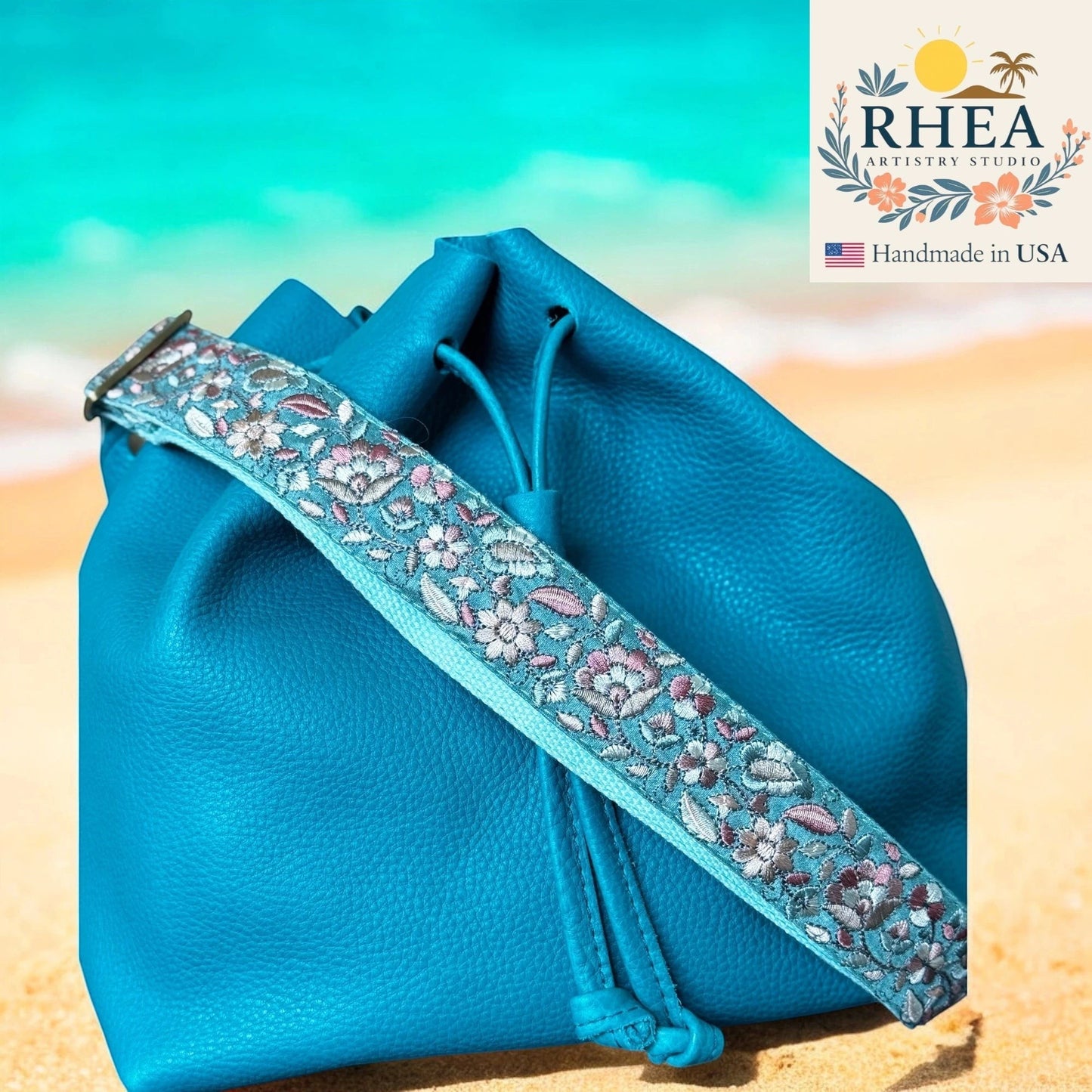Rhea Artistry Studio blue leather drawstring bag with a 1.5-inch adjustable embroidered floral fabric crossbody strap.