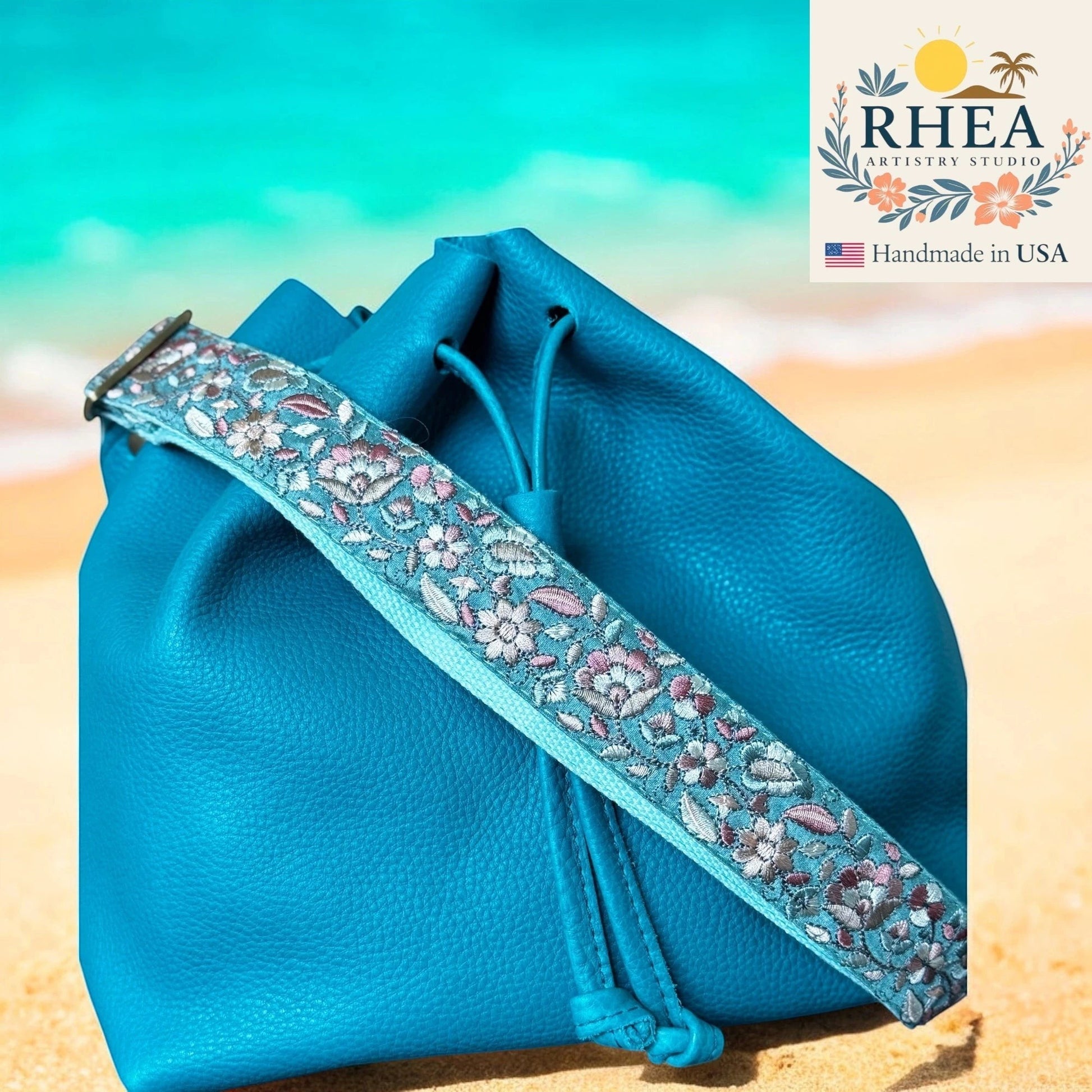 Rhea Artistry Studio blue leather drawstring bag with a 1.5-inch adjustable embroidered floral fabric crossbody strap.