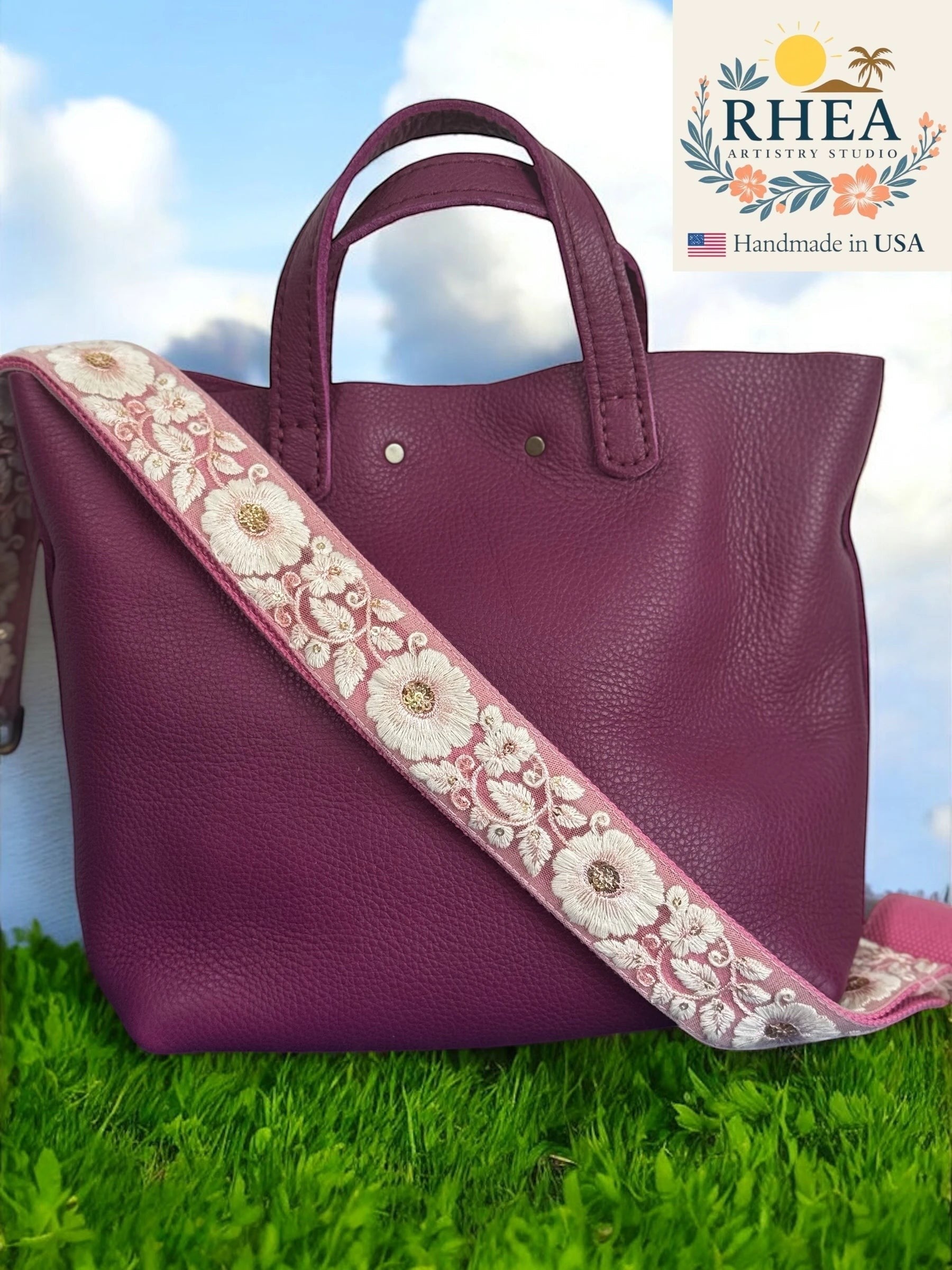 Rhea Artistry Studio plum leather tote with a 1.5-inch adjustable crossbody strap featuring white floral embroidery on a pink background.
