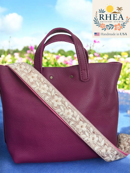 Rhea Artistry Studio plum flower embroidered crossbody strap with brushed brass hardware and adjustable length.