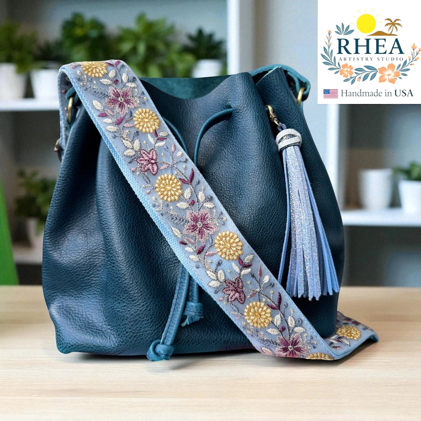 Rhea Artistry Studio 2-inch wide crossbody strap with blue floral embroidery, adjustable, made from lace and cotton webbing.