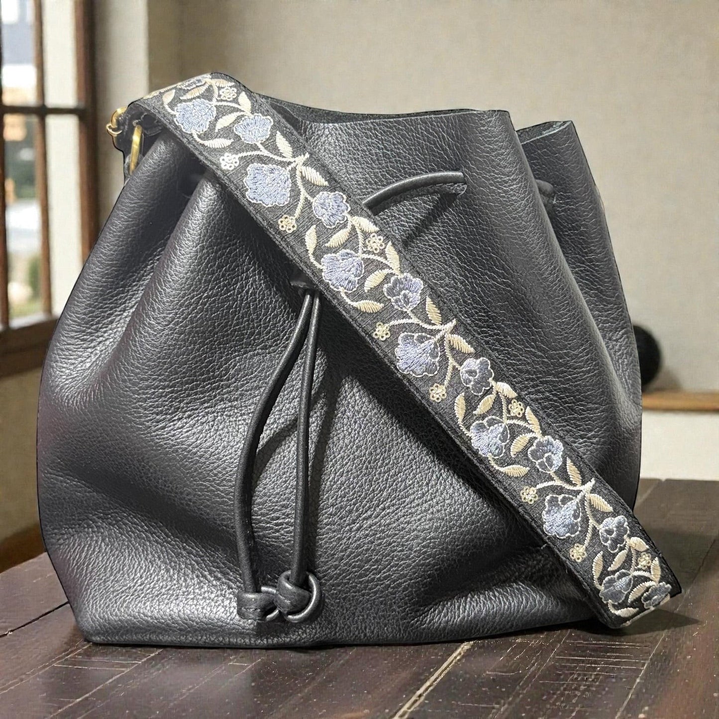 Rhea Artistry Studio Sierra Bloom embroidered crossbody strap with blue floral pattern on cotton webbing, 1.5-inch wide, adjustable 30-54 inches.
