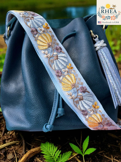 Rhea Artistry Studio light blue crossbody strap with embroidered floral and shell pattern, brass hardware, and tassel detail.