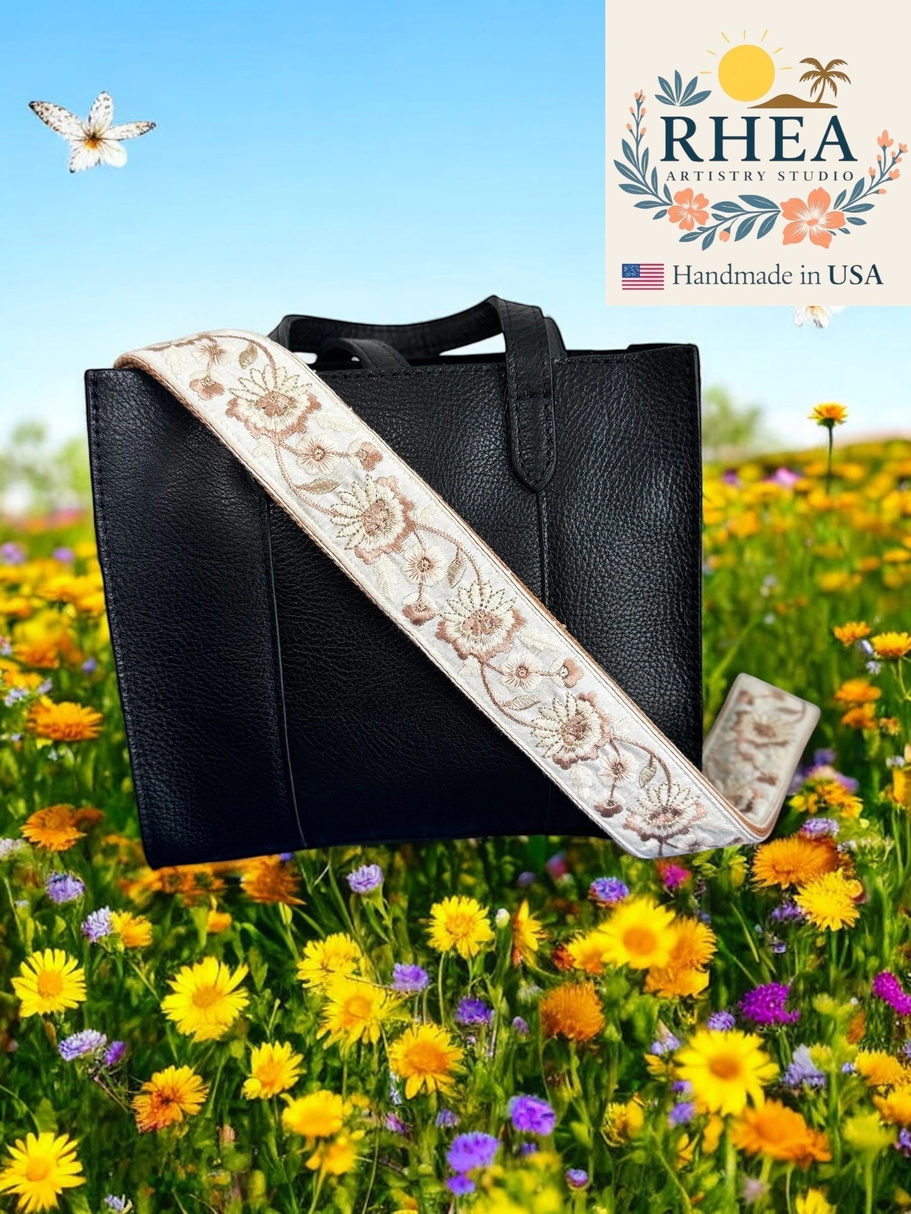 Rhea Artistry Studio cream crossbody strap with floral embroidery and brushed brass hardware on a black bag.