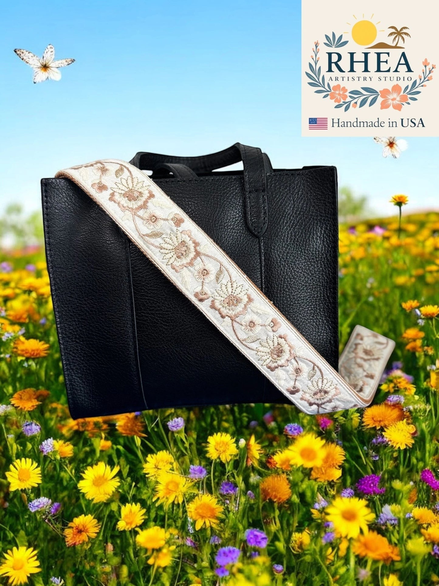 Rhea Artistry Studio cream and gold embroidered 2-inch wide crossbody strap with floral pattern on a black leather tote bag.