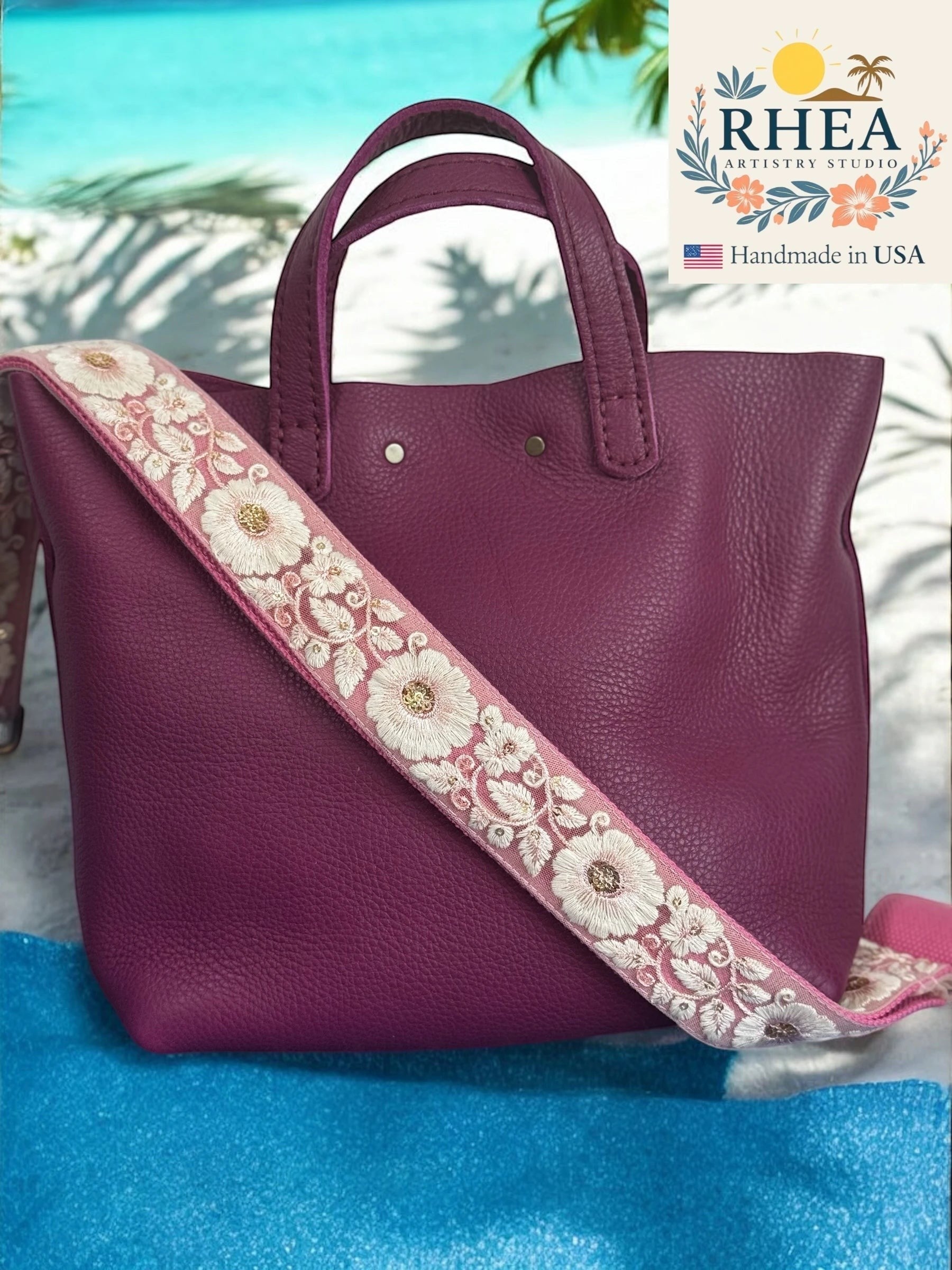 Rhea Artistry Studio plum leather tote with a 1.5-inch adjustable crossbody strap featuring white floral embroidery and brushed brass hardware.