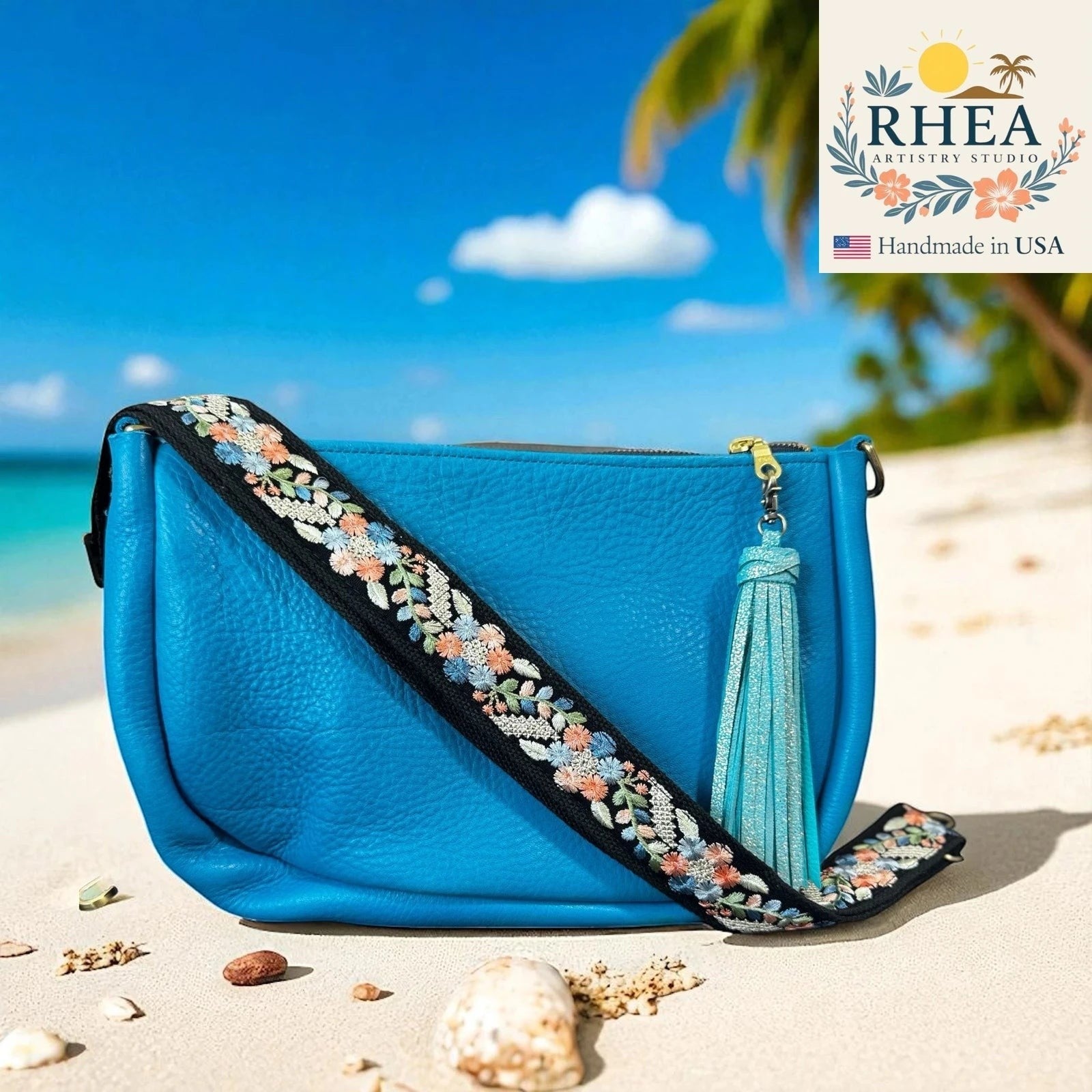 Rhea Artistry Studio blue crossbody bag with a 1.5-inch adjustable embroidered strap featuring silver, blue, and coral floral details.
