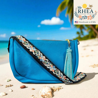 Rhea Artistry Studio blue crossbody bag with a 1.5-inch adjustable embroidered strap featuring silver, blue, and coral floral details.