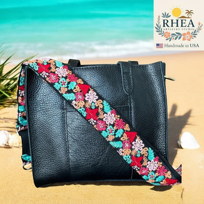 Rhea Artistry Studio black pebbled leather tote bag with a 2-inch wide adjustable crossbody strap featuring colorful floral embroidery in red, pink, and teal.