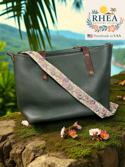 Rhea Artistry Studio crossbody strap with floral embroidery in pink, purple, and green on a light green background, with brushed brass hardware.