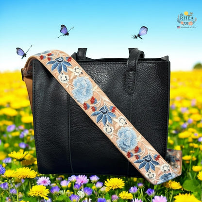 Rhea Artistry Studio 2-inch wide crossbody strap with blue floral embroidery on tan background, adjustable length, brushed brass hardware.