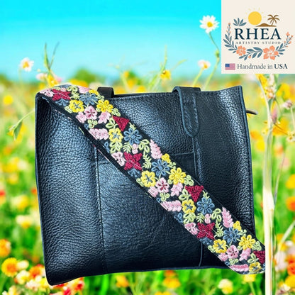 Rhea Artistry Studio black leather crossbody bag with a 2-inch wide adjustable strap featuring colorful floral embroidery and brass hardware.