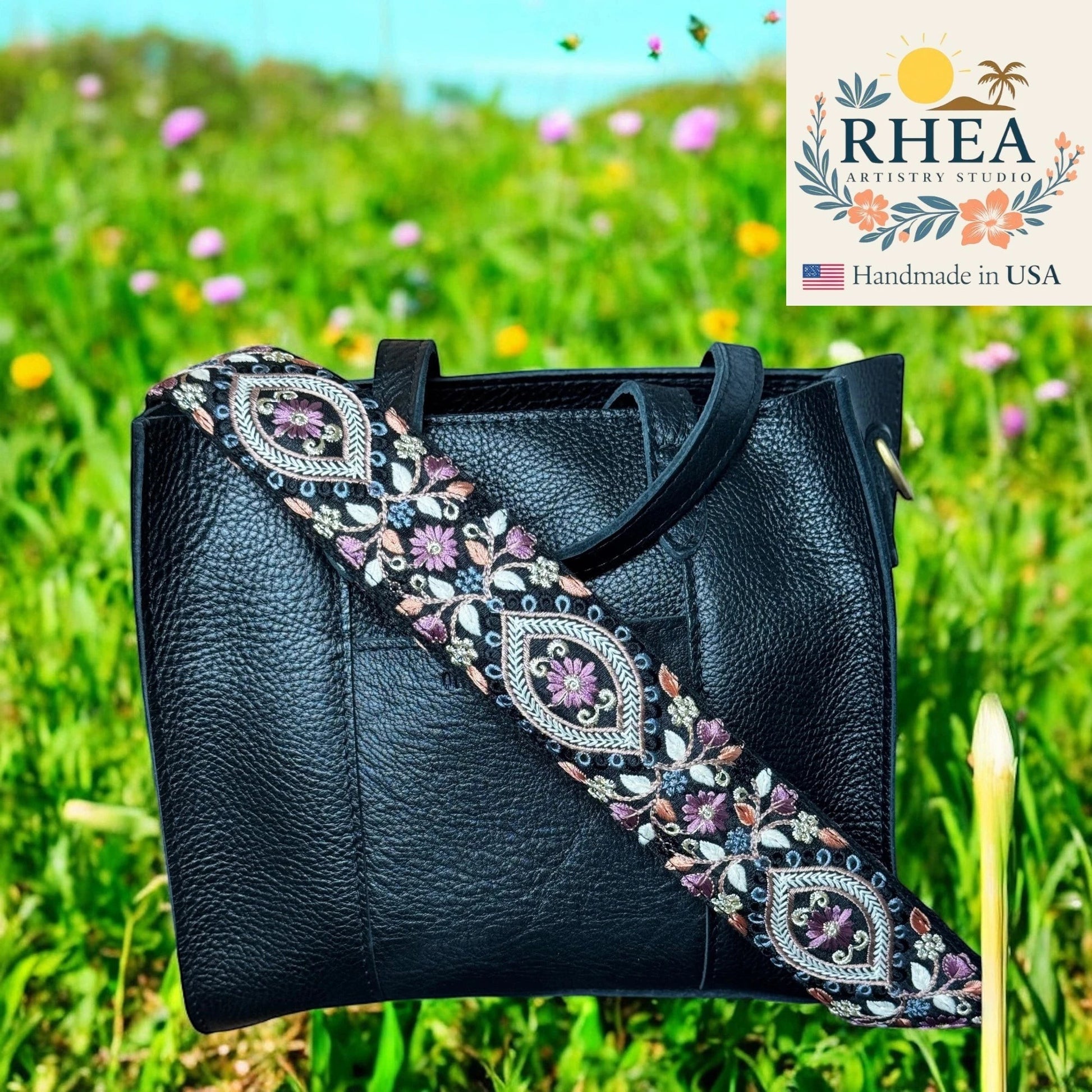 Rhea Artistry Studio black leather handbag with a 2-inch wide embroidered crossbody strap featuring floral and geometric patterns in purple, pink, and blue.