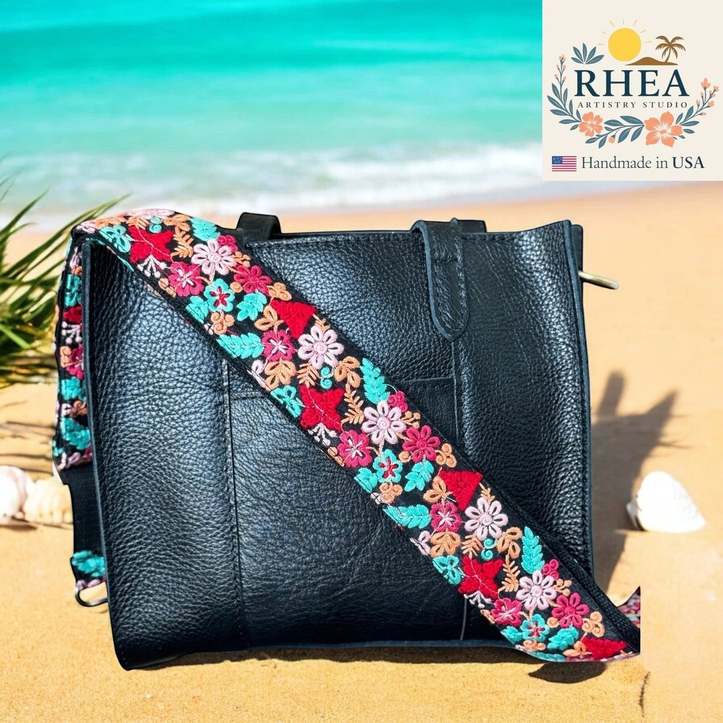Rhea Artistry Studio black leather tote with a 2-inch wide adjustable embroidered strap featuring colorful floral and leaf patterns.