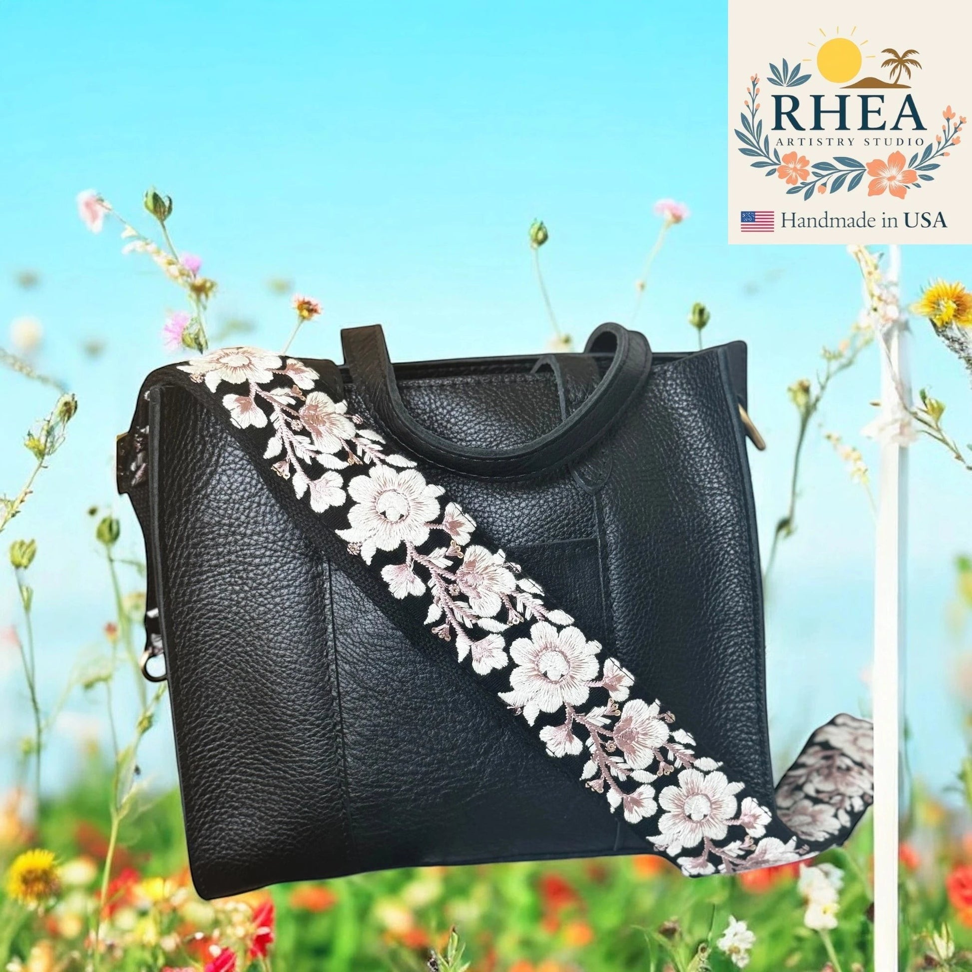 Rhea Artistry Studio black crossbody bag with a 2-inch wide adjustable strap featuring white and pink floral embroidery on black lace.
