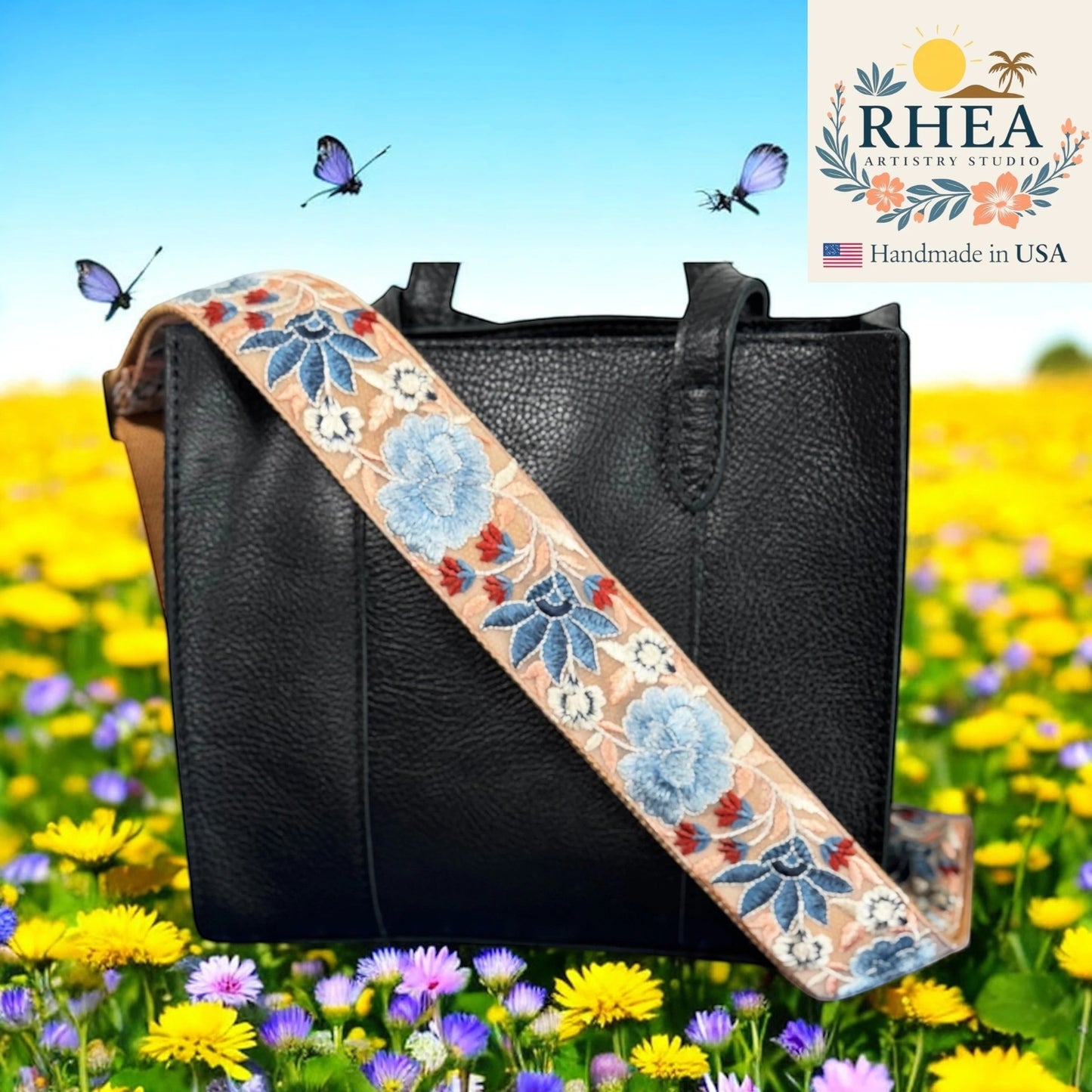 Rhea Artistry Studio 2-inch wide crossbody strap with blue floral embroidery on tan webbing, adjustable length, brushed brass hardware.