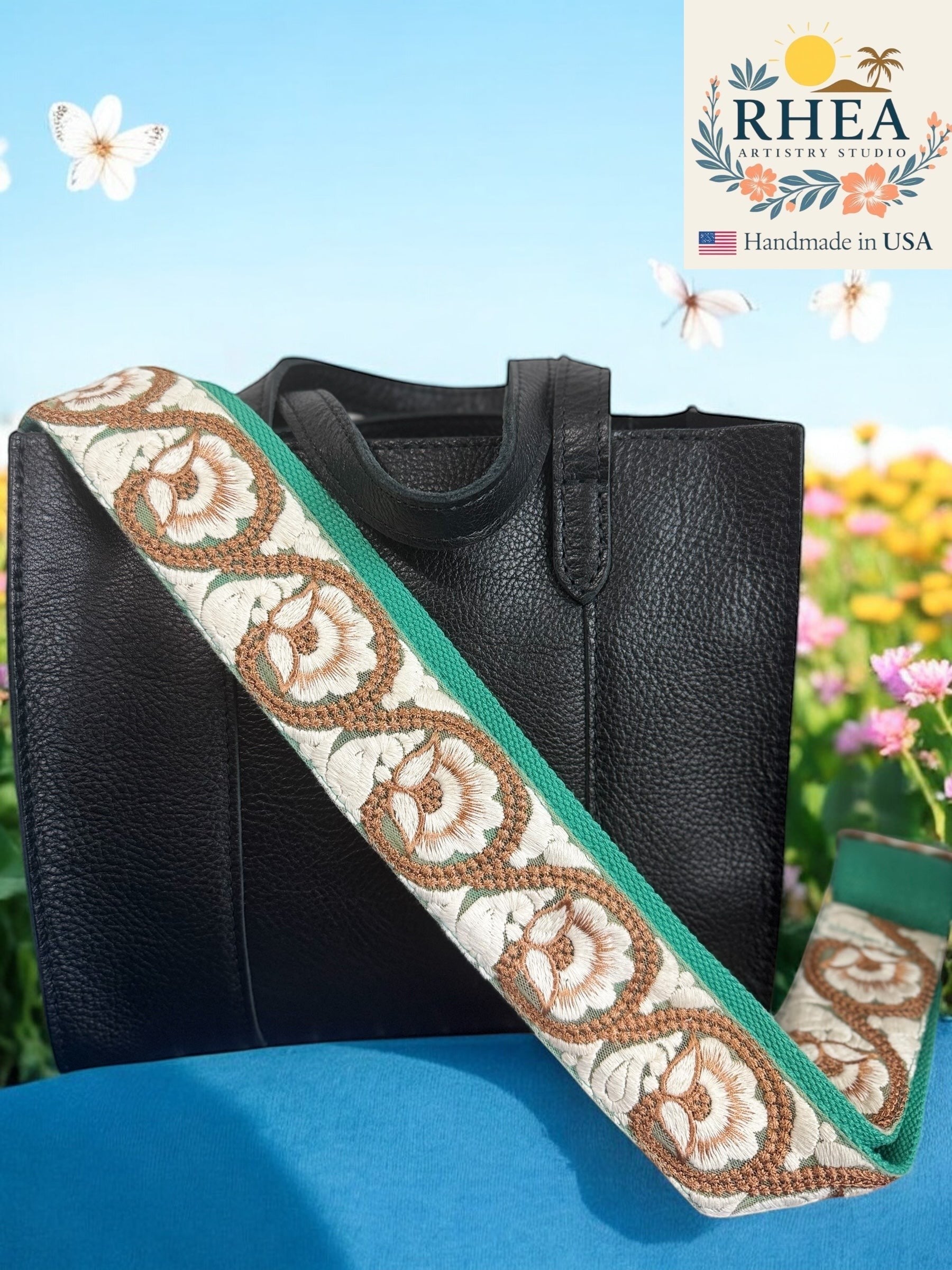 Rhea Artistry Studio 2-inch wide crossbody strap with white and brown floral embroidery on a green background, attached to a black handbag.