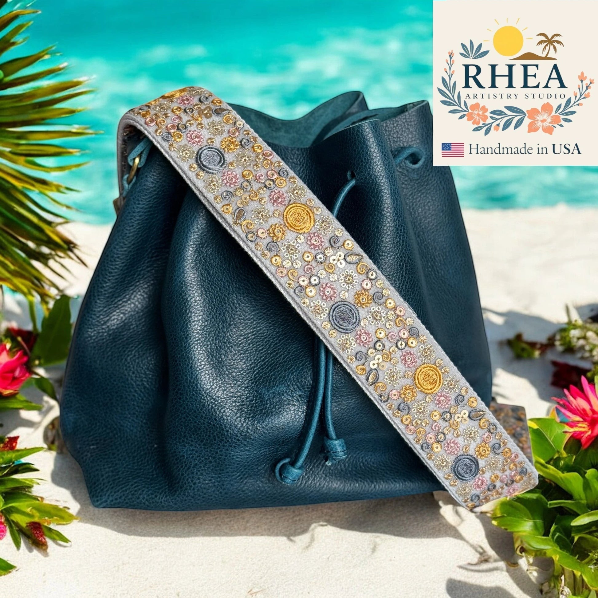Rhea Artistry Studio 2-inch crossbody strap with embroidered sun, moon, and floral motifs in gold, silver, and pink on grey fabric.