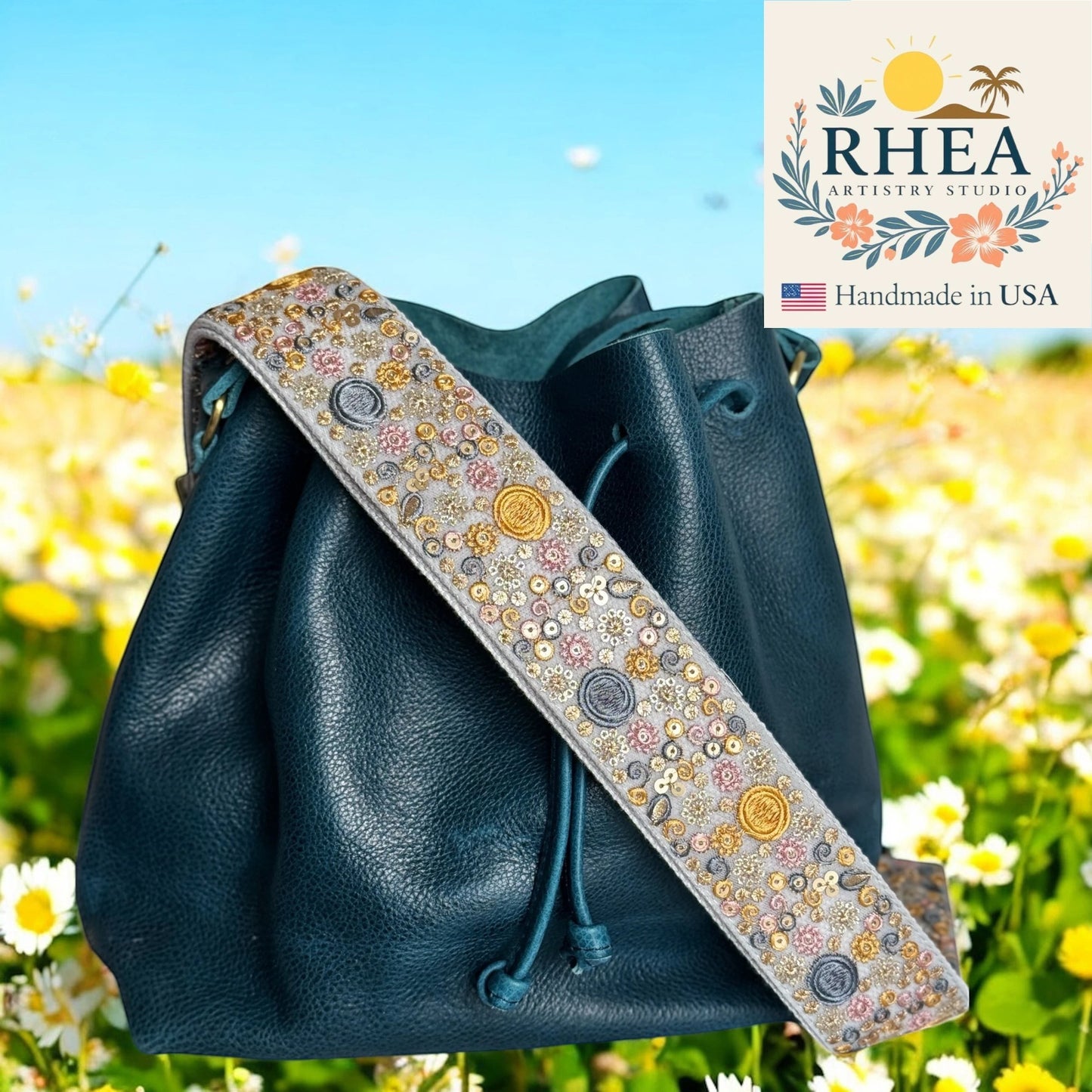 Rhea Artistry Studio 2-inch wide crossbody strap with intricate sun, moon, and floral embroidery in gold, pink, and grey.