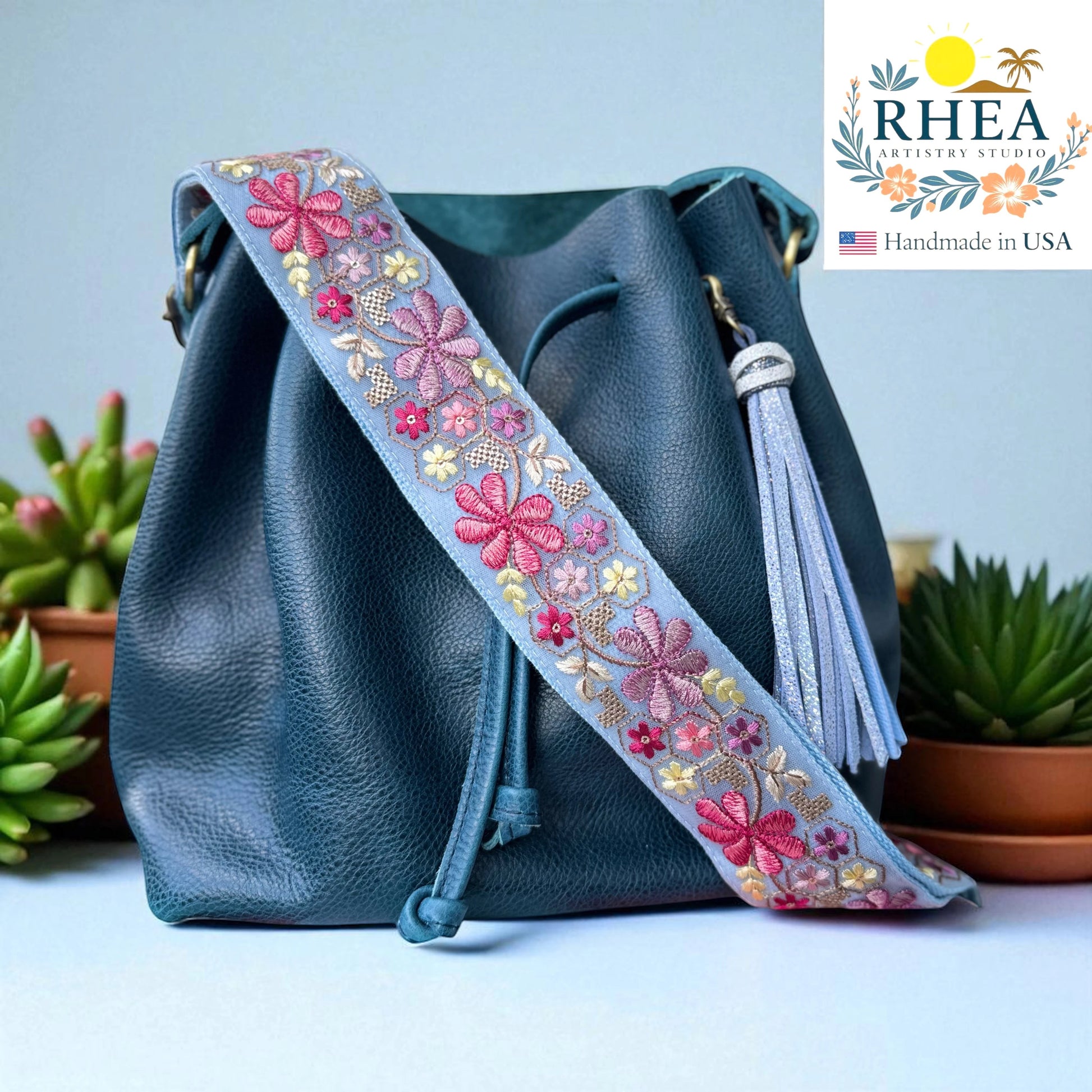 Rhea Artistry Studio light blue embroidered crossbody strap with pink and purple floral details, 2 inches wide, adjustable 30-54 inches.
