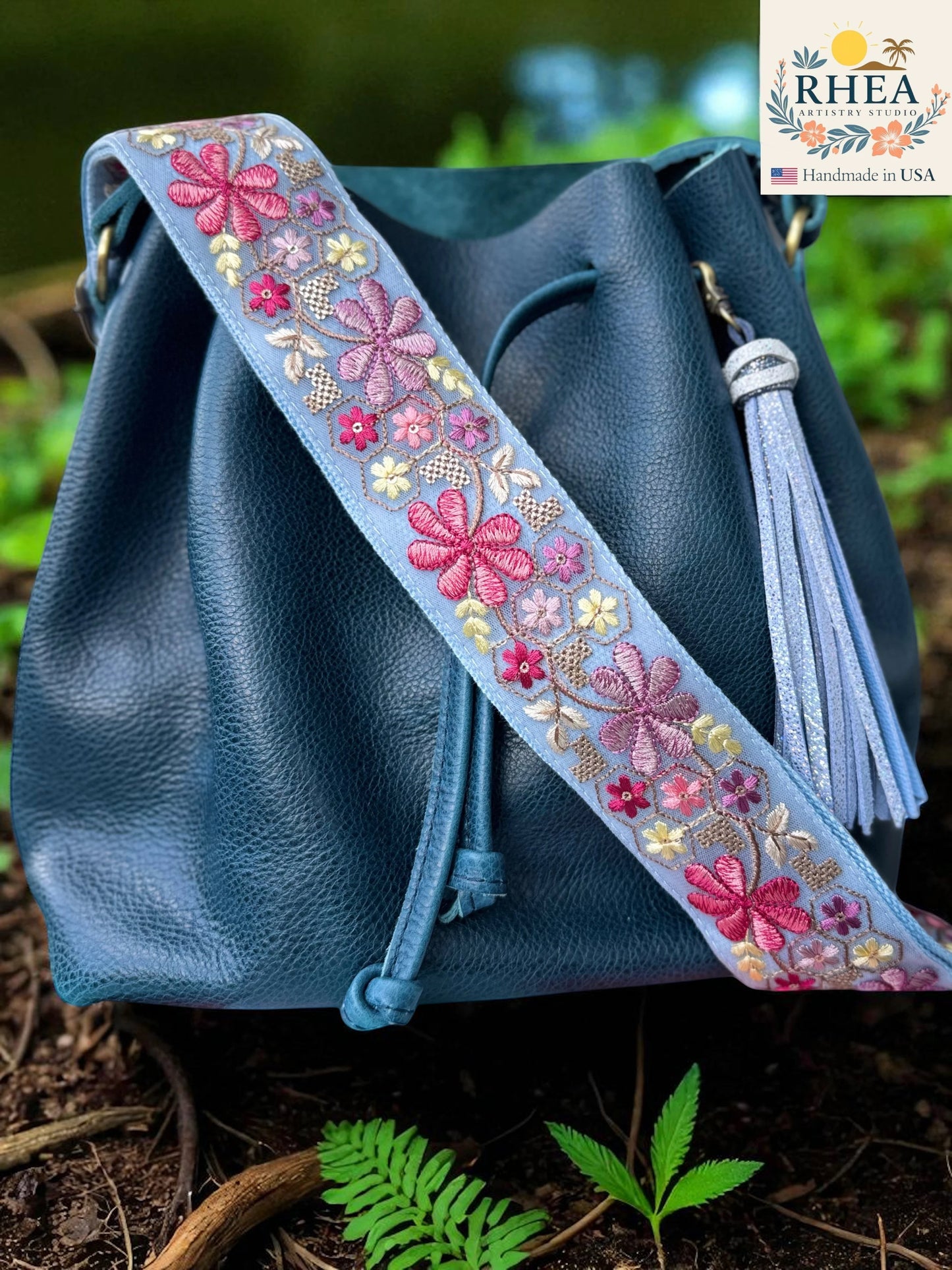 Rhea Artistry Studio light blue embroidered crossbody strap with pink, purple, and yellow floral details. Adjustable 2-inch width.