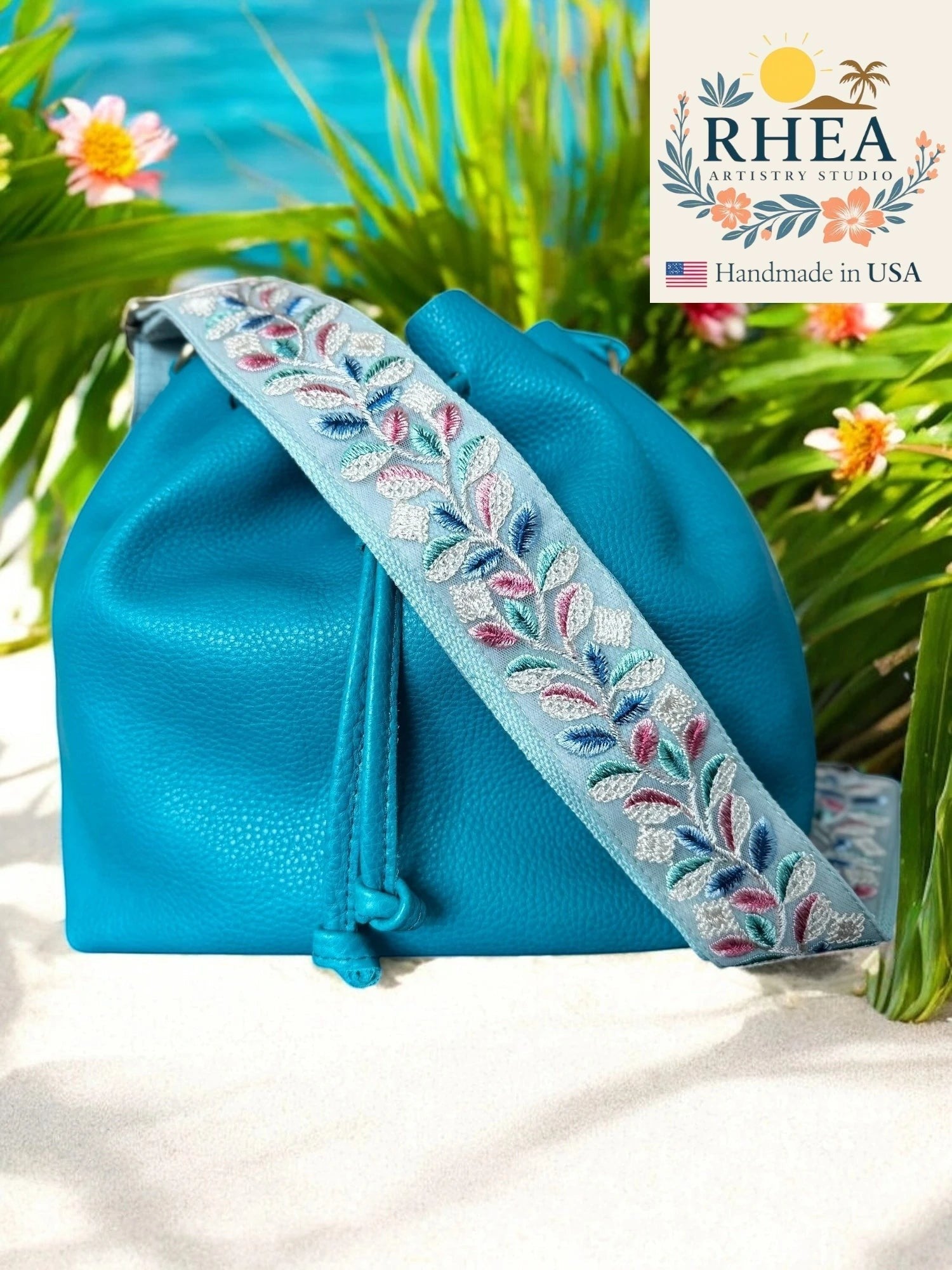 Rhea Artistry Studio light blue embroidered crossbody strap with floral vine pattern, brushed brass hardware, adjustable 30-54".