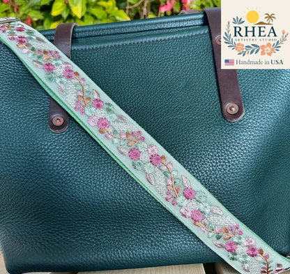 Rhea Artistry Studio 1.5-inch crossbody strap with mint green lace embroidery of pink flowers and green leaves, adjustable length, brushed brass hardware.
