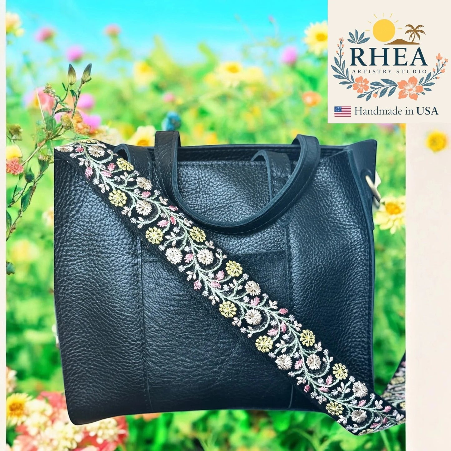 Rhea Artistry Studio black leather crossbody bag with a 1.5-inch adjustable strap featuring soft moss green, ivory, and blue floral embroidery.