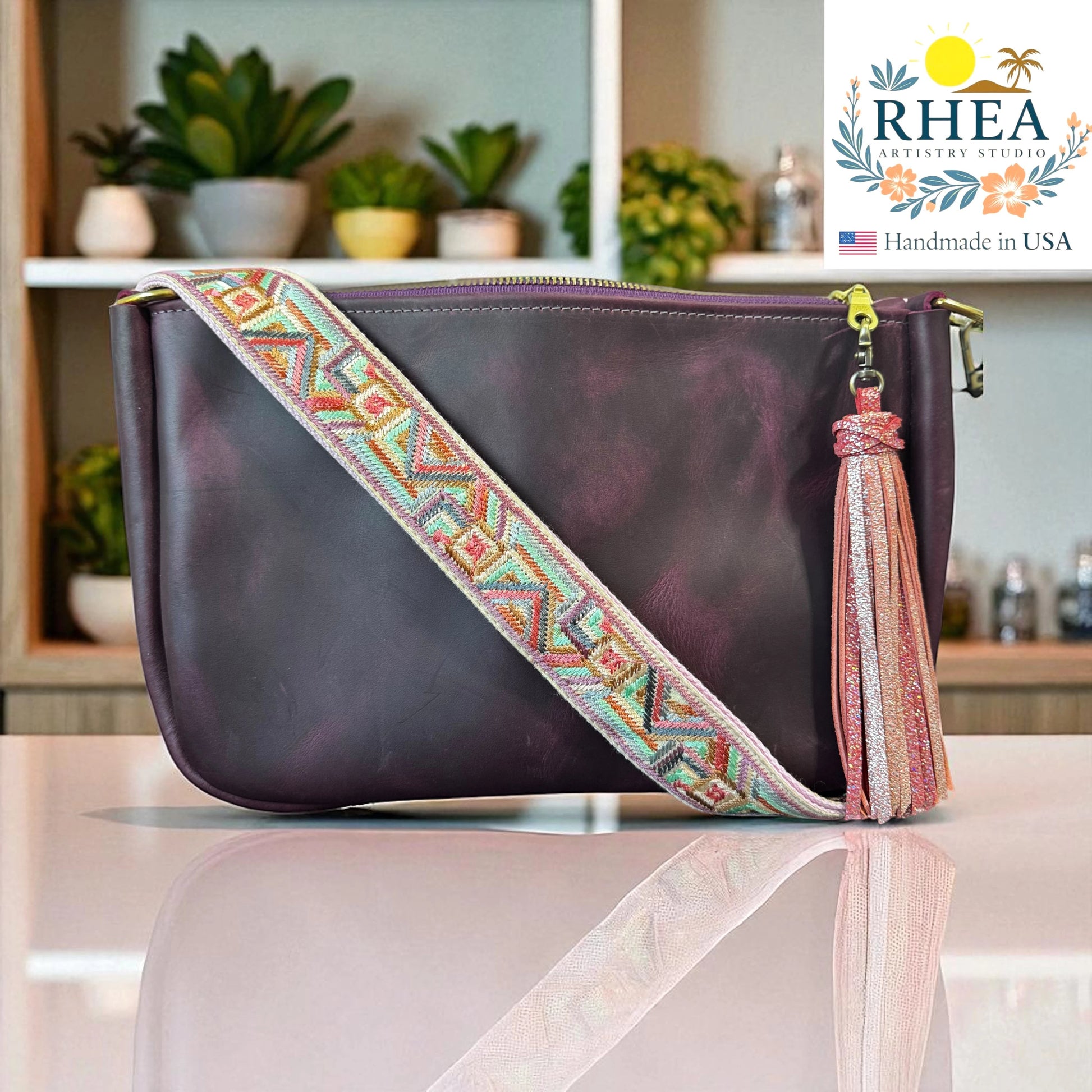 Rhea Artistry Studio 1.5-inch crossbody strap with geometric embroidery in pastel colors, featuring a pink glitter tassel and brushed brass hardware.