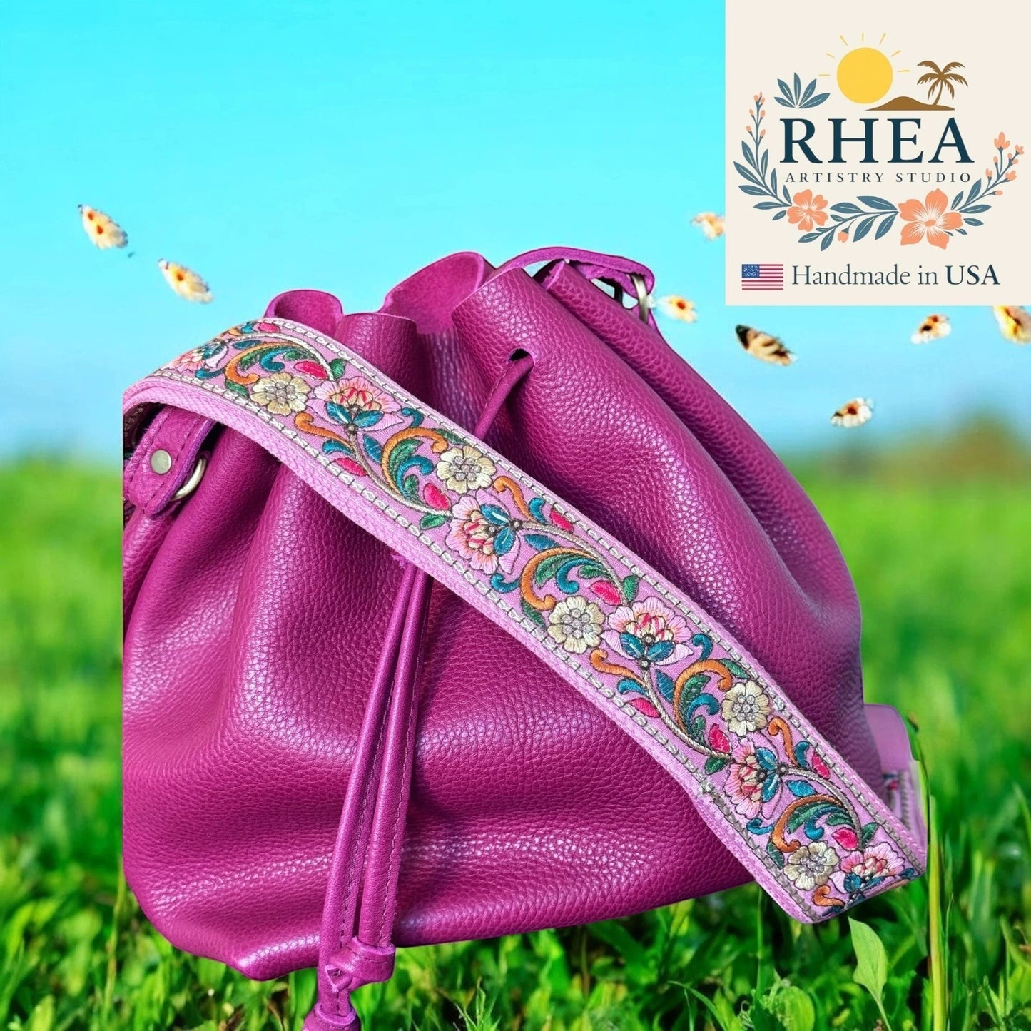 Rhea Artistry Studio 2-inch wide crossbody strap with vibrant floral embroidery on pink lace, attached to a magenta leather bucket bag.