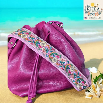 Rhea Artistry Studio 2-inch wide crossbody strap with floral embroidery in pink, green, and yellow on cotton webbing. Adjustable 30-54 inches.