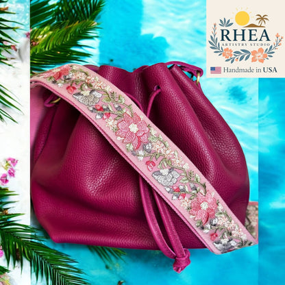 Rhea Artistry Studio pink embroidered crossbody strap with floral pattern on a magenta leather bucket bag.