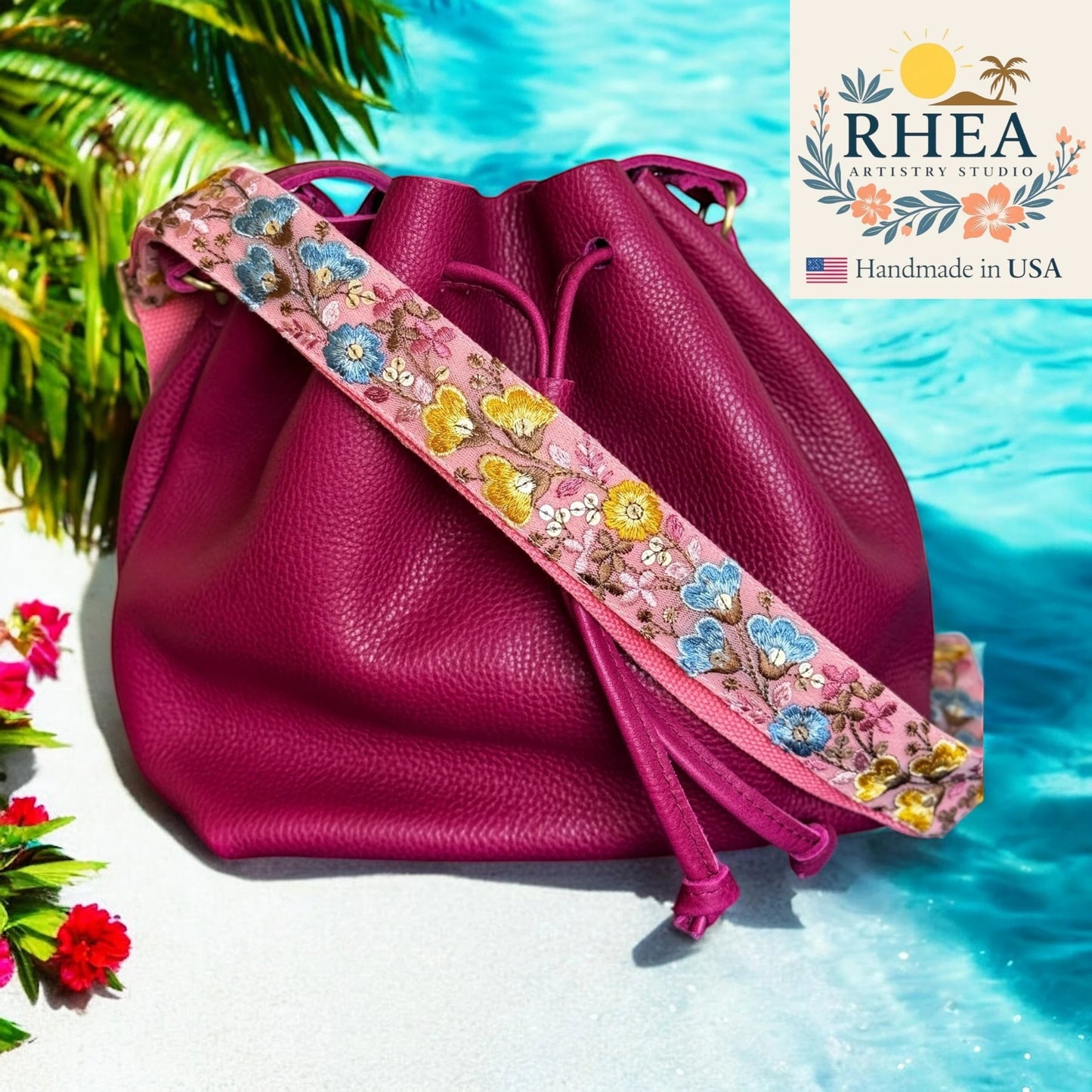 Rhea Artistry Studio pink embroidered crossbody strap with floral and butterfly motifs on a magenta leather bucket bag.