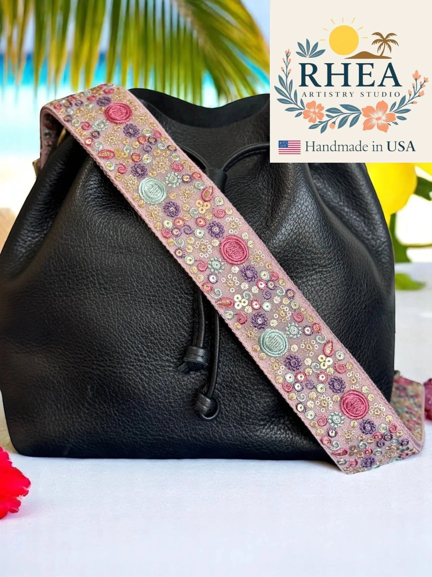 Rhea Artistry Studio pink embroidered crossbody strap with sun, moon, and floral motifs, 2-inch width, adjustable length, and brushed brass hardware.