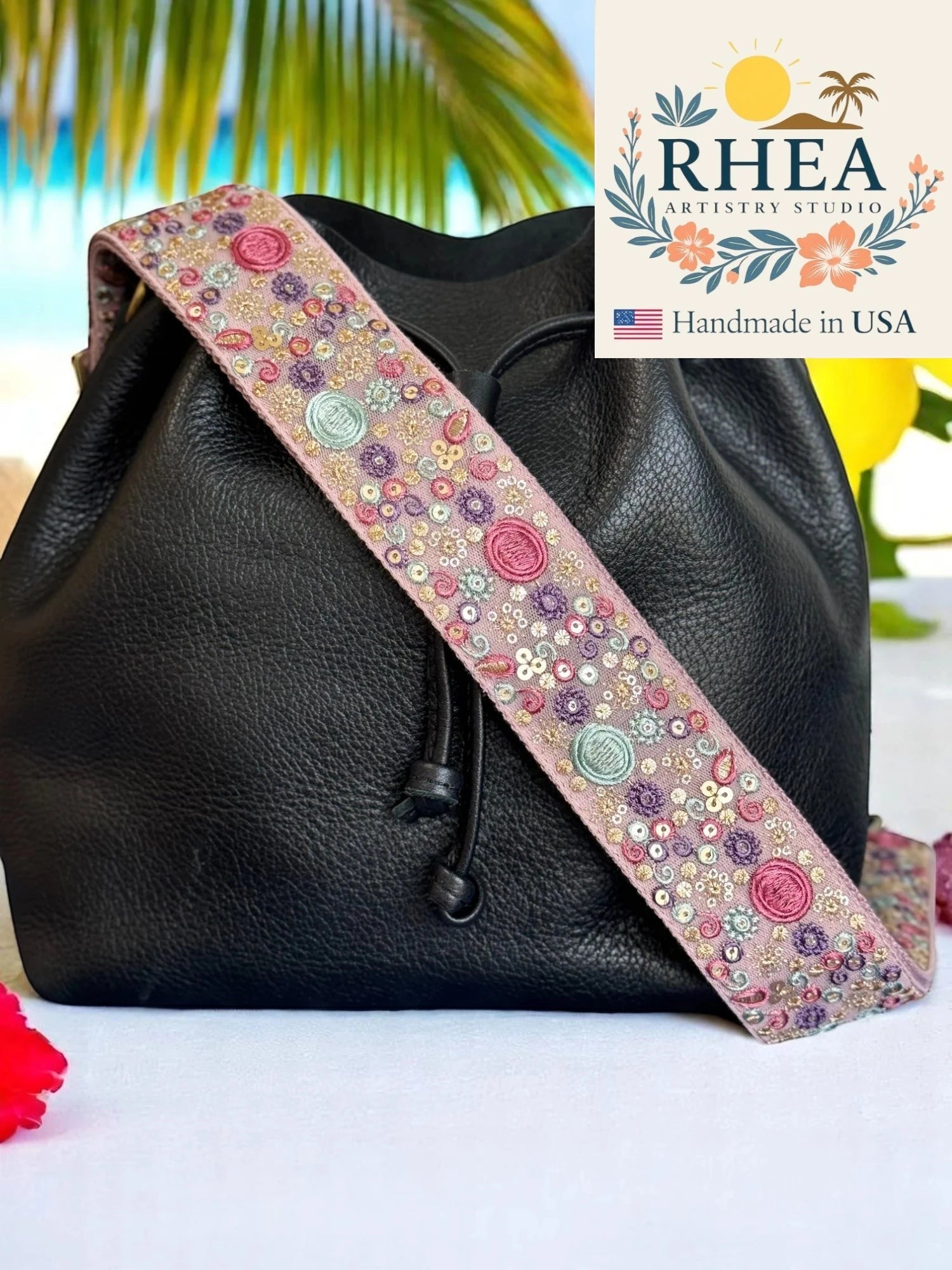 Rhea Artistry Studio pink embroidered crossbody strap with sun, moon, and floral motifs, 2-inch width, adjustable length, and brushed brass hardware.