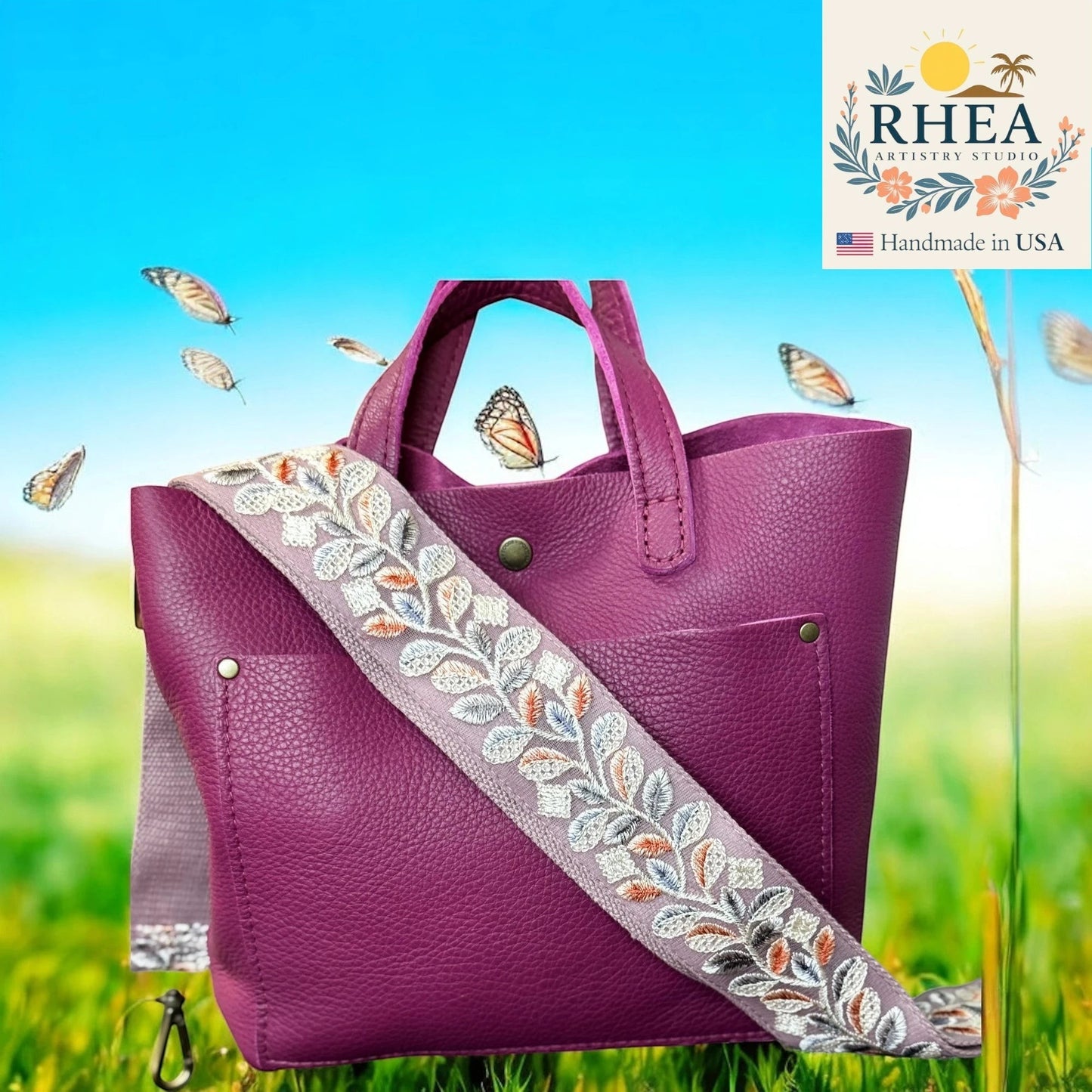 Rhea Artistry Studio 2-inch crossbody strap with floral embroidery in grey, white, orange, and blue on a purple leather bag.