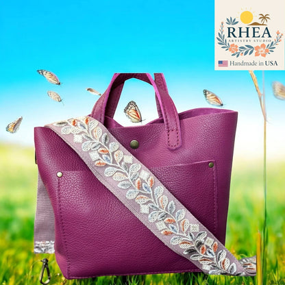 Rhea Artistry Studio 2-inch crossbody strap with floral embroidery in grey, white, orange, and blue on a purple leather bag.