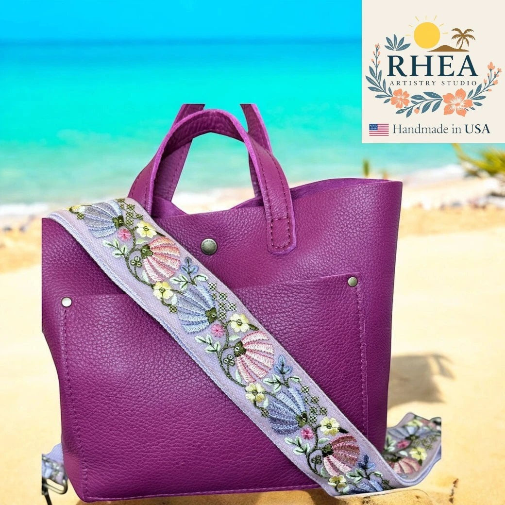 Rhea Artistry Studio purple leather tote with a 2-inch wide adjustable crossbody strap featuring embroidered floral and seashell details on a light purple background.