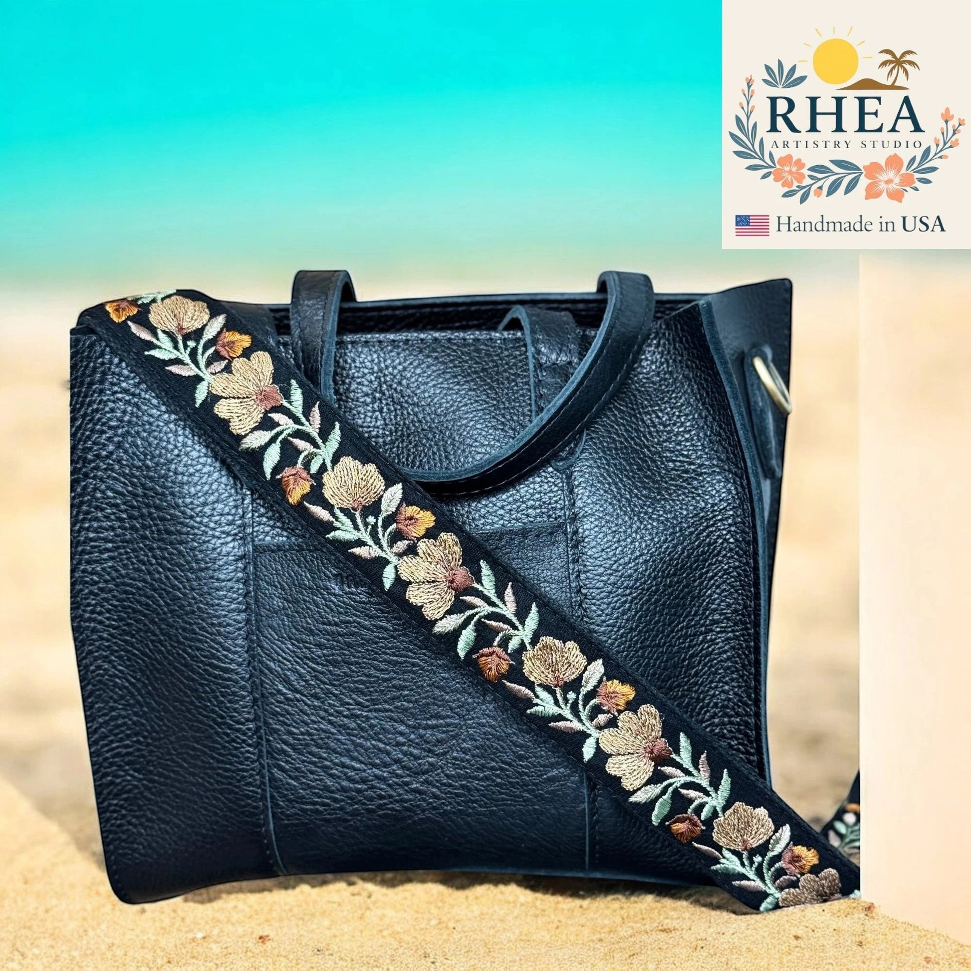 Rhea Artistry Studio black leather crossbody bag with a 1.5-inch adjustable strap featuring terracotta, sage, and ivory floral embroidery.