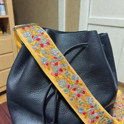 Rhea Artistry Studio yellow embroidered lace crossbody strap with floral design and brass hardware on a black bucket bag.