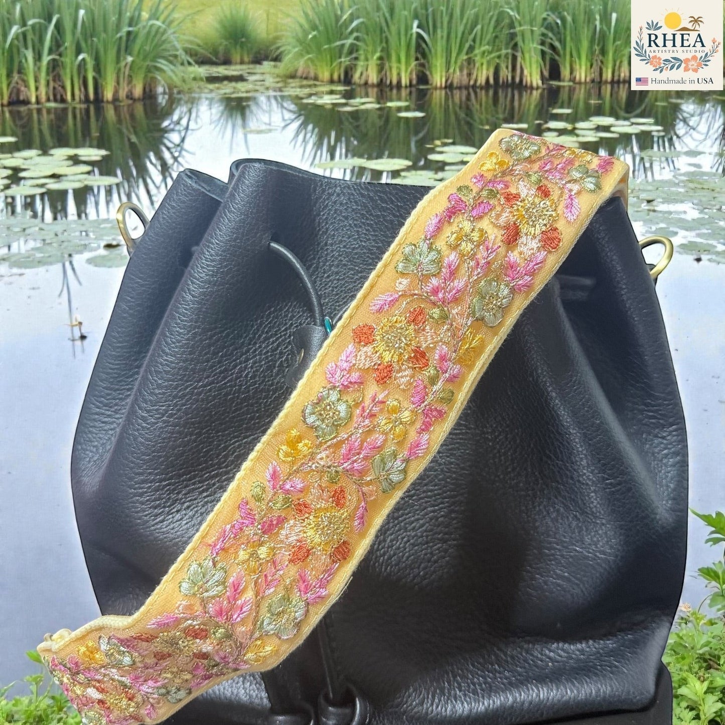 Rhea Artistry Studio yellow embroidered lace crossbody strap with floral details and brass hardware on a black bucket bag.