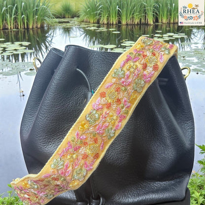 Rhea Artistry Studio yellow embroidered lace crossbody strap with floral details and brass hardware on a black bucket bag.